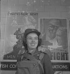 Service féminin de la Force aérienne, années 1940. Une femme non identifiée en uniforme, portant un sac sur la poitrine, devant les nouvelles affiches de l'armée du Canada [between 1940-1949]