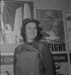 Service féminin de la Force aérienne, années 1940. Une femme non identifiée en uniforme, portant un sac sur la poitrine, devant les nouvelles affiches de l'armée du Canada [between 1940-1949]
