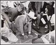 La légende canadienne de la musique country Wilf Carter grave l'empreinte de ses mains et pieds dans la pierre sur la « Walkway of Stars » de l'avenue Stephen après son récent spectacle du 10 juillet au Stephen Avenue Mall de Calgary [between 1965-1970].