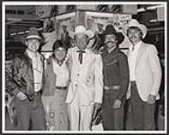 Wilf Carter lors d'une séance d'autographes à Calgary. De gauche à droite : Kevin Roe (représentant commercial, RCA), Beverley Williams (Événements spéciaux, La Baie), Wilf Carter, Ken Malvin (acheteur, La Baie), Terry Carson (directeur commercial, RCA) [ca 1983]
