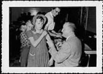 Snap-shot of a male doctor giving a young girl a vaccine. Nurses and Nursing. Department of Citizenship and Immigration, Information Division [between 1930-1960]