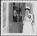 Instantané d'une infirmière montrant un nouveau-né à trois jeunes femmes par la vitrine d'une pouponnière. Infirmières et soins. Ministère de la Citoyenneté et de l'Immigration, division de l'information [between 1930-1960]
