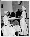 Deux infirmières préparant un plateau d'outils dans la salle d'approvisionnement centrale des services, St. Joseph Hospital, Victoria. Infirmières et soins. Ministère de la Citoyenneté et de l'Immigration, division de l'information [entre 1930-1960]