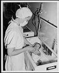 Infirmière autorisée nourrissant un bébé dans une pouponnière. Edmonton. Infirmières et soins. Ministère de la Citoyenneté et de l'Immigration, division de l'information [between 1930-1960]