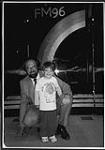 Portrait de Chuck Phillips, personnalité de Drive au FM96 lors de la Kindentification, avec un jeune garçon. Londres [between 1980-1990]