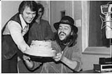 Greg Stewart, directeur des programmes du FM/96 (à gauche), remet à Chuck Mangione un gâteau en forme de chapeau lors de son passage au studio alors qu'il était à Montréal pour donner un concert [entre 1980-1990]