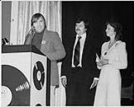 Bob Cousins, Roy Hennessy, and an unidentified woman speaking from the RPM Awards podium [entre 1970-1974].