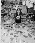 Unidentified female Box Office employee sitting in a large pile of mail and tossing it in the air. The mail involves the band The Who and their song The Kids Are Alright. Vancouver [entre 1969-1979].