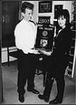 Frank Davies and Annette Ducharme holding a diamond award for Tom Cochrane's record Mad Mad World. The Music Publisher (TMP). Toronto [between 1991-1992].