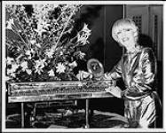 E. Dee Gold standing next to a vinyl record, a miniature piano and a floral display March 24, 1979