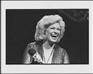 Portrait of Carroll Baker laughing and holding a microphone [entre 1975-1985]