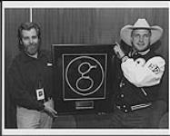 Portrait of Garth Brooks and Deane Cameron holding an award (?) comprised of Brooks' signature 'g' made of rope in a frame [ca 1995]