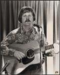  Portrait de Dave Baker qui tient une guitare [between 1965-1975]