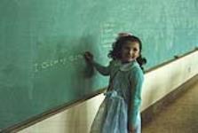 Jeune fille debout en classe près d'un tableau noir n.d.