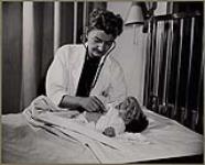 Female doctor examining a baby with a stethoscope [entre 1930-1960].