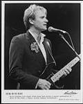 Photo publicitaire de Sting au micro jouant de la guitare durant un concert Bring de On the Night 1985