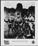 Publicity portrait of Tenpole Tudor dressed in armour and standing in front of a castle - (l to r) Gary Long, Munch Universe, Eddie Tudorpole, Dick Crippen, Bob Kingston [entre 1980-1983].