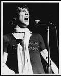 Murray Head wearing a scarf and singing into a microphone [entre 1975-1980].