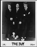 Press portrait of The Jam wearing dark suits and leaning against a wall n.d.