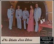 Photo publicitaire du Sheila Ann Show : quatre hommes en complets bleus et une femme vêtue d'une robe rose debout dans un restaurant [entre 1970-1979].