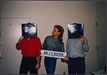Paris Black debout avec deux hommes tenant son album devant leurs visages à la station radio 88,7 CJOM [between 1990-1991].
