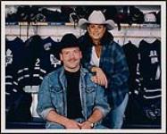 Terri Clark and Wendel Clark posing in front of Wendel Clark's hockey equipment [between 1996-2000].