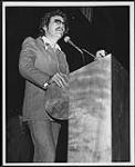 Gordon Lightfoot speaking at a podium [entre 1977-1978].