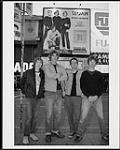 The recording artists Sloan standing in front of a promotional billboard [ca 1999].