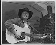 Musicien qui porte un chapeau de cowboy et joue de la guitare [between 1980-1990].