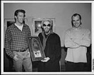 Ashley MacIsaac presented with a platinum award for the album "hiTM how are you today?" in Charlottetown, PEI. Pictured left to right are: Allan Reid (A&M / Island / Motown V.P. of Marketing), Ashley MacIsaac and John Reid (President, A&M / Island / Motown Records of Canada) 10 février 1996