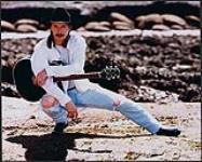 Rick Tippe portant un jeans déchiré et un chapeau de cowboy et tenant une guitare [entre 1994-1998].