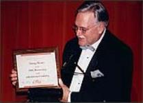 Paul Corbin, Vice President of Music Industry Relations and Gaylord Entertainment, holds an award which reads: Tommy Hunter on his 50th Anniversary in the entertainment industry [ca 1997].