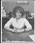 Faye LaBuick, assise à son bureau [entre 1970-1975].