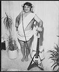 Sammy Jo Romanoff du magazine RPM, vêtu d'un costume, tient une guitare Gibson Flying V [entre 1965-1970].