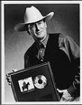 Ian Tyson portant un chapeau de cow-boy et prenant une pose avec un prix d'album [between 1990-1993].