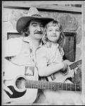 Michael T. Wall, playing guitar, and his daughter Sarah Anne who is playing a toy guitar [entre 1980-1987].