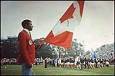 Harry Jerome portant le drapeau canadien lors des cérémonies d'ouverture des premiers Jeux d'été du Canada, à Halifax-Dartmouth août 1969.