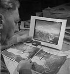A man examining photographs for an atlas 1950