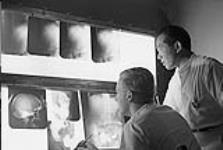 Le docteur Tok Djien Liem se tient derrière le docteur Fred MacDonald pour examiner des rayons X 1954