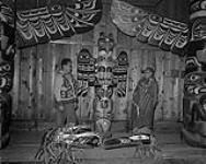 Deux Autochtones [L'homme de droite est Mungo Martin] de part et d'autre d'un mât totémique. Intérieur 1955