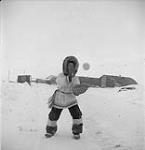 An adolescent Inuit boy in winter clothing playing baseball. Iqaluit, 1958