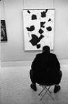 A man sitting in front of the painting "The Seagull" by Paul-Emile Borduas 1960