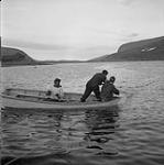 Two Inuit men stretching a nylon gill net across a small stream's mouth 1960