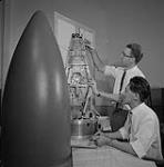Laboratoires du Conseil de recherches pour la défense. John Mar (assis) et Gordon Philips avec la coiffe qui contiendra les instruments pour mettre à l'essai le déploiement ingénieux de l'antenne de 75 pieds du satellite canadien « TopsideSounder » mars 1961