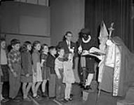 Santa Claus visits school children at the Werl National Defence School of the 4th Canadian Infantry Brigade. The role of "Saint Nick" was played by S/Sgt. Aurel Belanger and looking on is school principal Paul Paquette 6 December 1958.