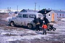 [Inuit men pushing a van by a barber shop]. Original title: Es pushing a car [between 1958-1968]