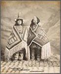 [Studio portrait of Stene-Tu and Kaw-Claa, Tlingit women wearing naaxein (Chilkat blankets)]. Original title: Stene-Tu and Kaw-Claa, two Thlinget women in Chilkat blankets 1906