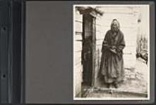 [Elderly First Nations woman smoking a pipe outside a wooden building] 1903