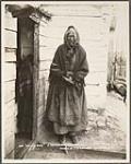 [Elderly First Nations woman smoking a pipe outside a wooden building]. Original title: 'An old wife', a typical Northerner 1903