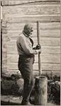 [Anishinaabe man, Peter Jones, pounding corn grains with a pestle in a mortar at Wiikwemkoong First Nation] [ca. 1916]